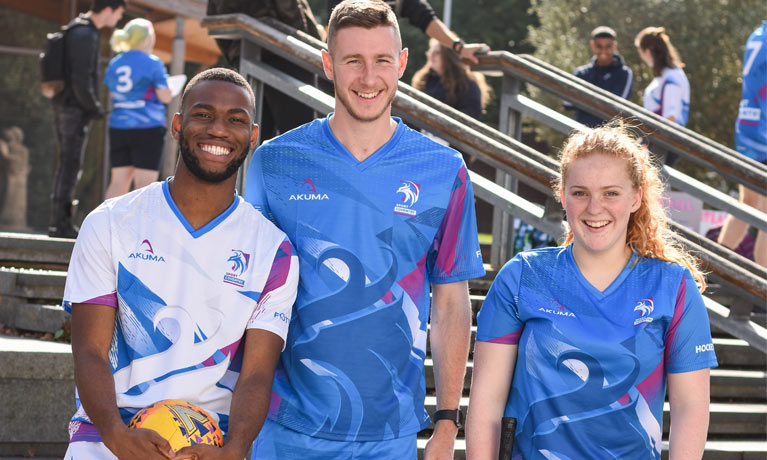 Three students smiling in sports kit.