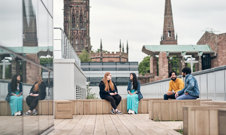 Students sat chatting in the rooftop garden at The Hub, with the cathedral spire in the background.