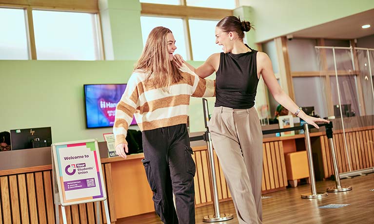 Two students walking through reception smiling and laughing